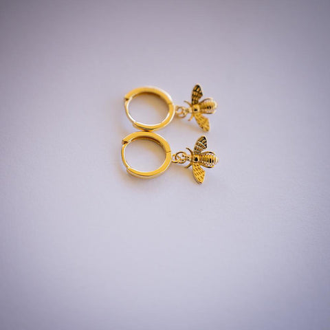 Gold hoop earrings with bee dangle on white background