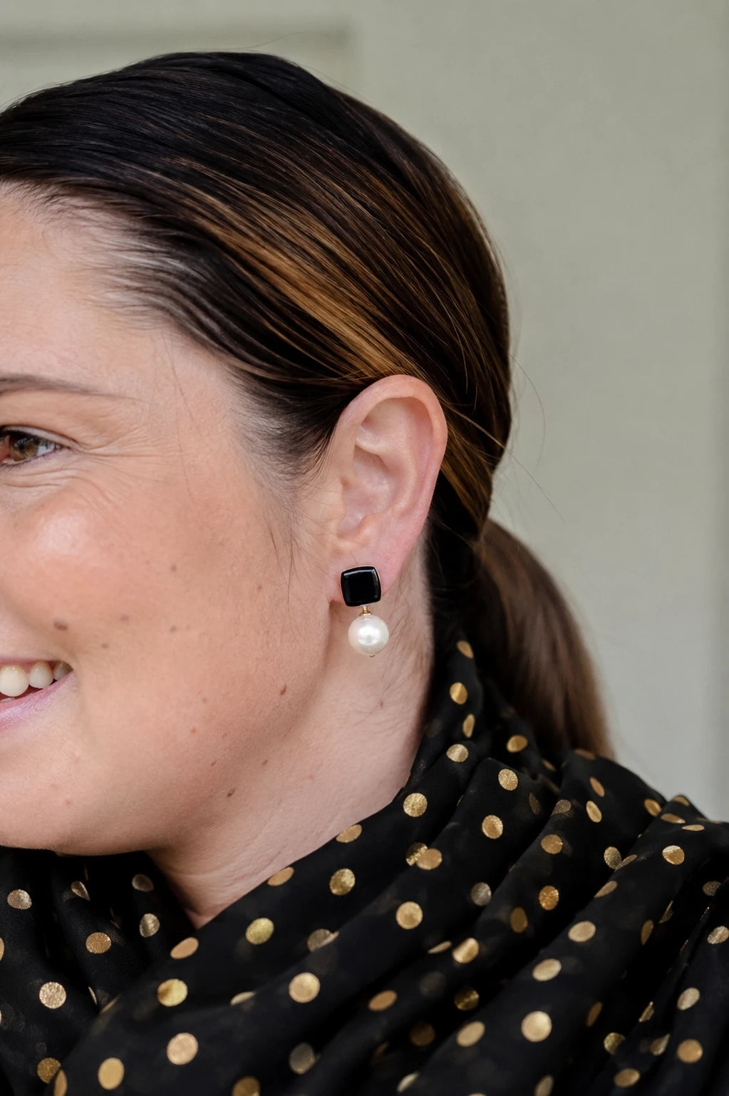 Woman smiling wearing Felicity black enamel square stud earrings with faux pearl drop by Greenwood Designs, styled with a black and gold top