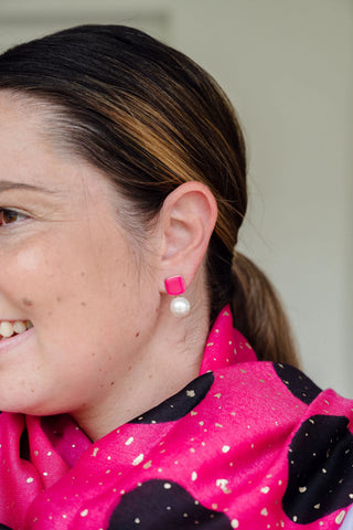 Woman smiling wearing Felicity bright pink enamel square stud earrings with faux pearl drop by Greenwood Designs, styled with a hot pink and black scarf