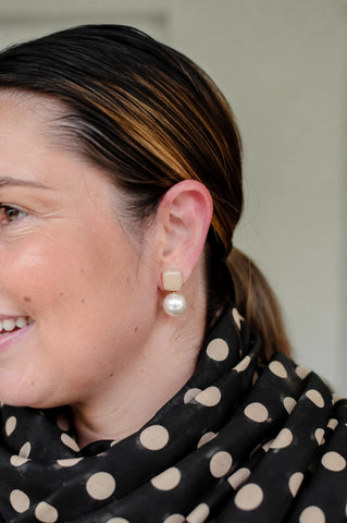 Woman smiling wearing Felicity cream enamel square stud earrings with faux pearl drop by Greenwood Designs, styled with a black and beige polka dot scarf