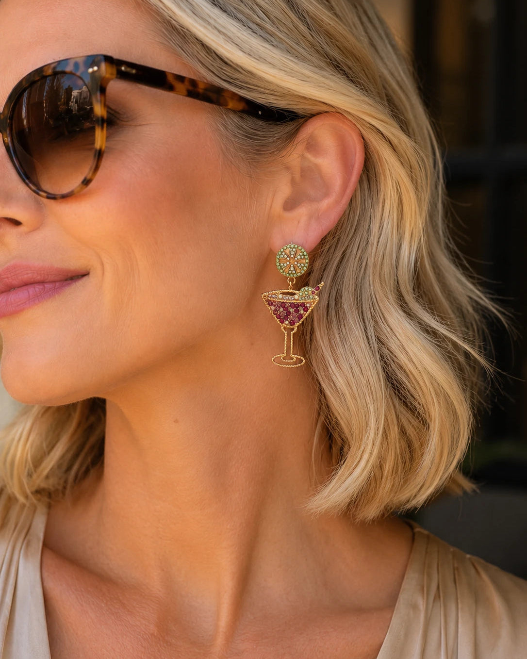 Woman wearing Martini Time pink and green crystal martini glass drop earrings by Greenwood Designs, styled with tortoiseshell sunglasses and a nude top