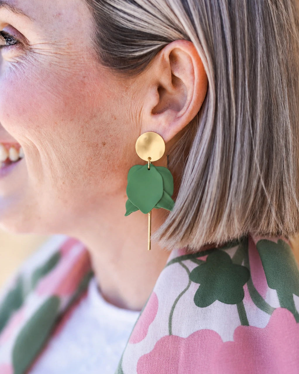 Close-up of a person wearing green earrings with floral patterned clothing.