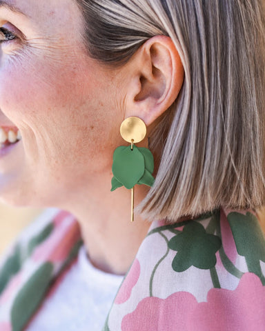 Close-up of a person wearing green earrings with floral patterned clothing.