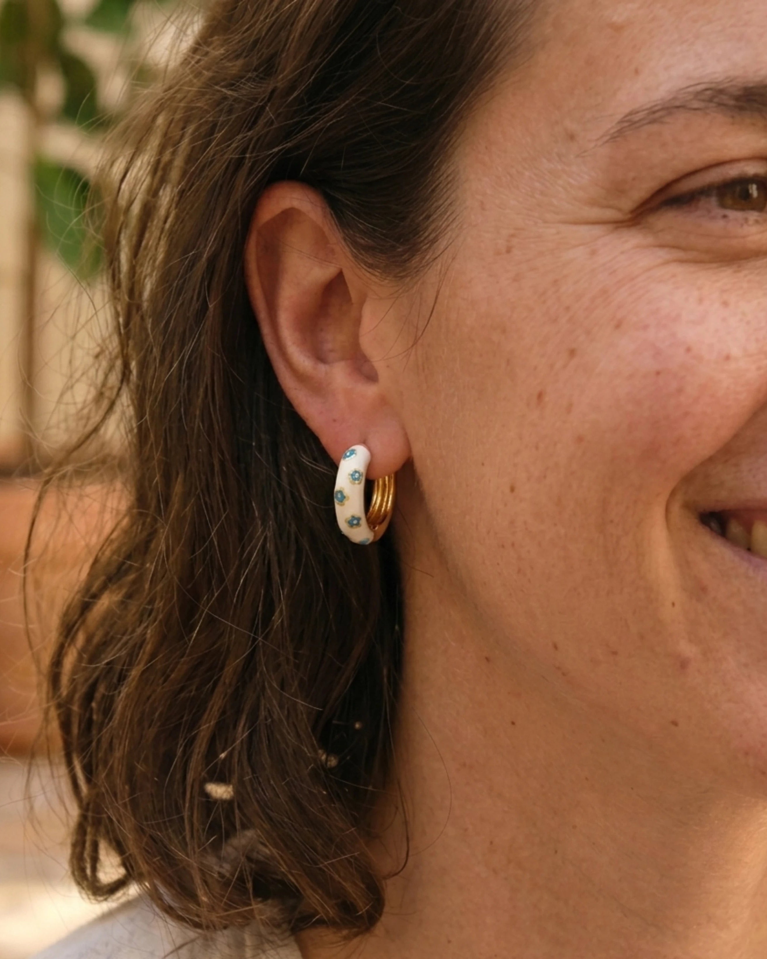 Woman wearing white enamel gold hoop earrings with blue flower pattern