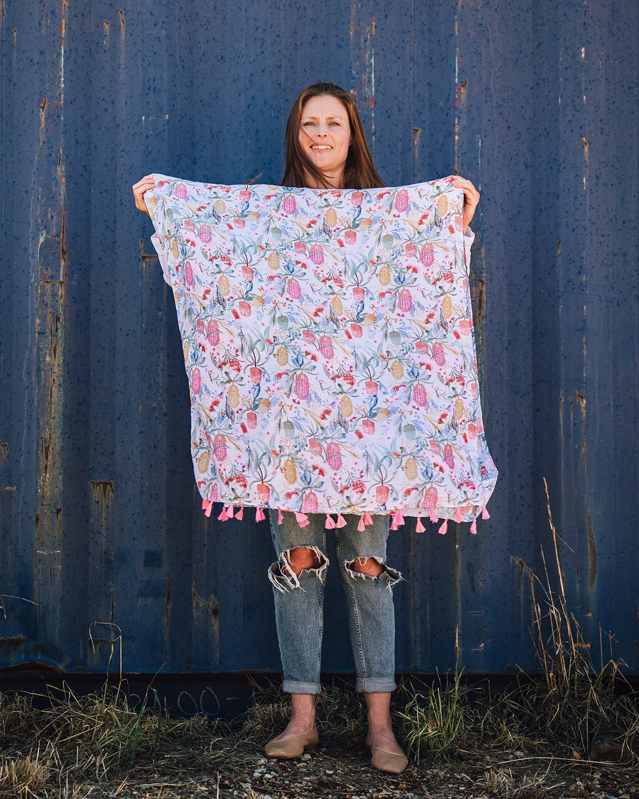 Abby Australiana Women's Scarf: Australian botanical print featuring waratahs, bottle brushes, and eucalypts in pinks, greens, blues, and muted yellows on a white background. Charming pink tassels at each end. Polyester blend for a soft and comfortable we