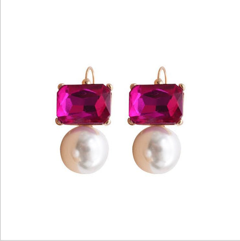 A pair of earrings featuring bright pink rectangular crystals above faux pearls, with gold plated earring hooks and settings.