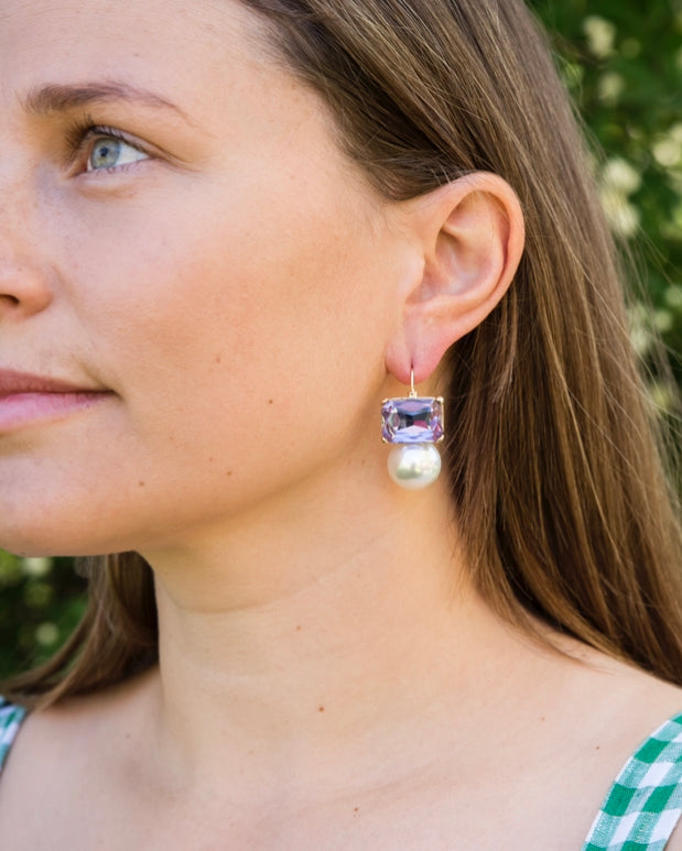 Woman wearing Maggie violet rectangular crystal and faux pearl drop earrings by Greenwood Designs outdoors
