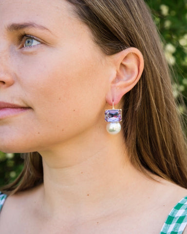 Woman wearing Maggie violet rectangular crystal and faux pearl drop earrings by Greenwood Designs outdoors